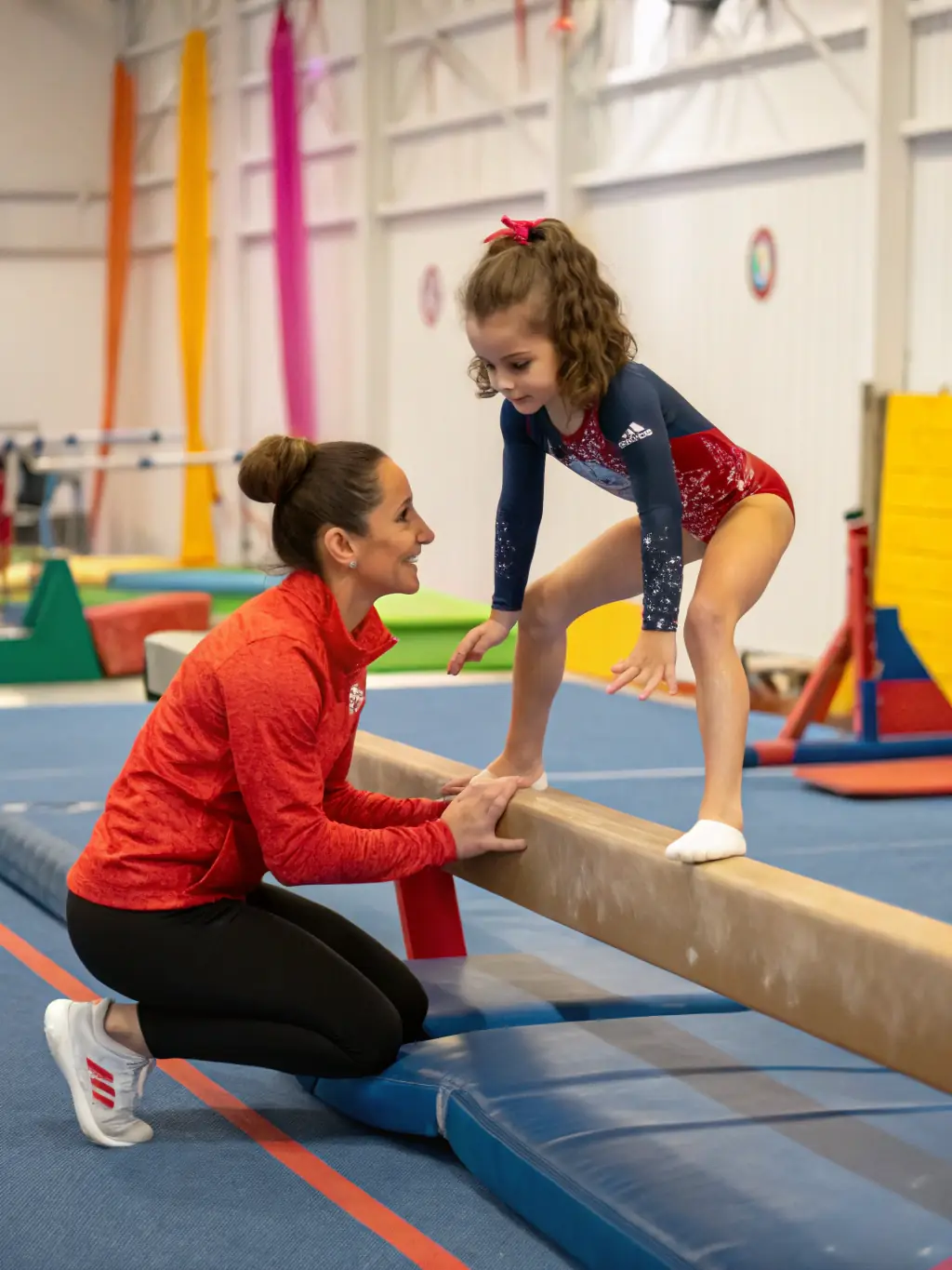 A photograph capturing a gymnastics coach providing personalized instruction to a young gymnast, showcasing the one-on-one attention and expert guidance at AGVM.